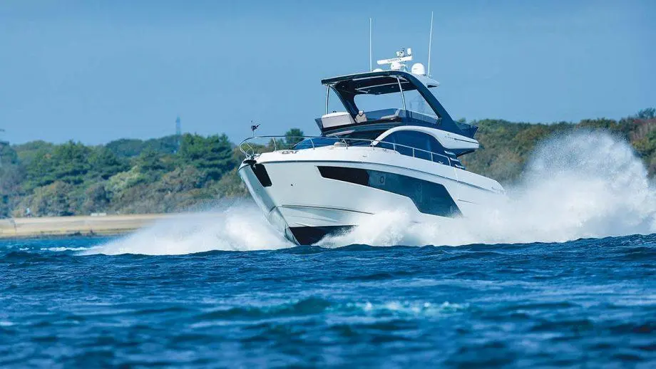 Luxury boat speeding through blue water, creating sprays, with trees and a clear sky in the background.